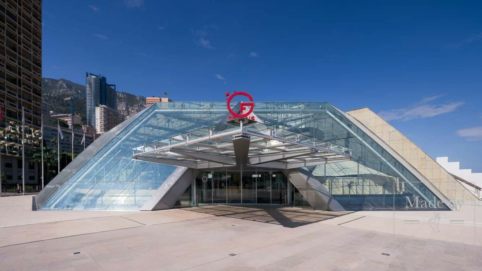 The glass pyramid entrance of the Grimaldi Forum convention centre in Monaco under a clear blue sky.