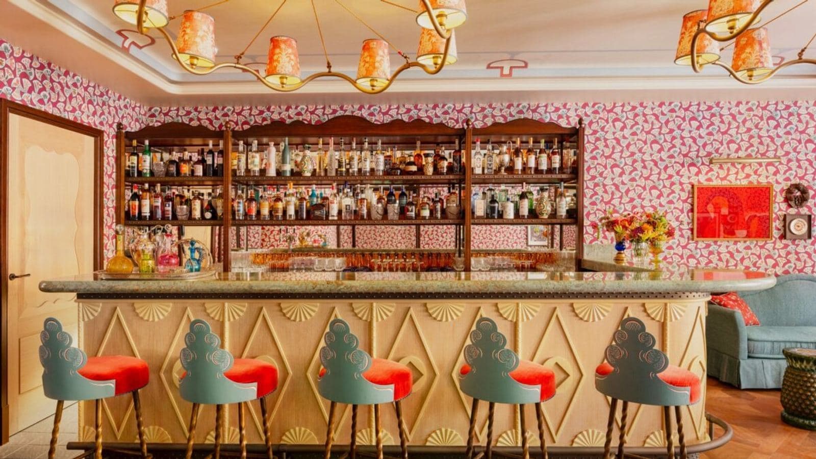The maximalist bar at Le Grand Mazarin, with patterned wallpaper, ornate chandeliers and carved bar stools upholstered in orange velvet.