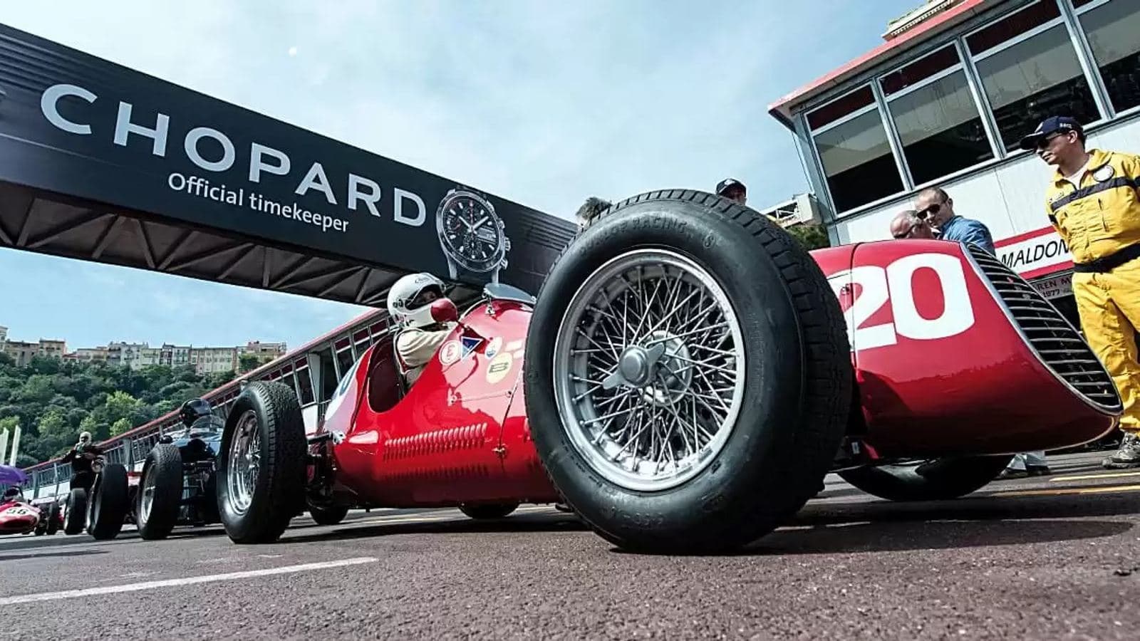 A vintage red racing car with wire wheels passing beneath a Chopard Official Timekeeper banner at the Grand Prix de Monaco Historique.