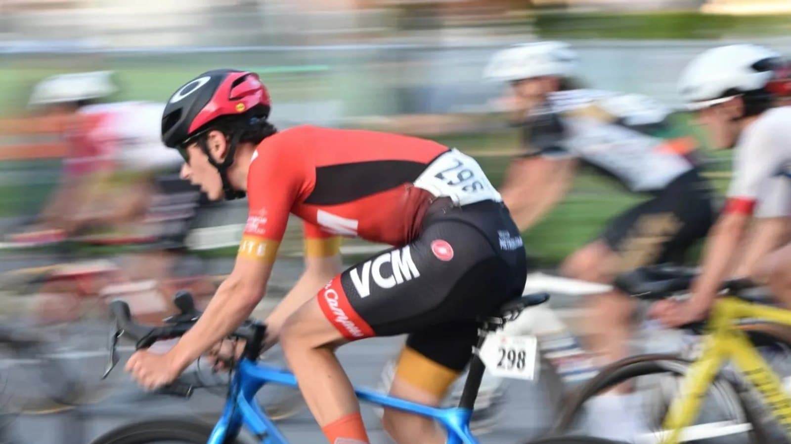 A road cyclist in racing kit leaning into a turn among a pack of riders, evoking La Vuelta's Grand Depart from Monaco.