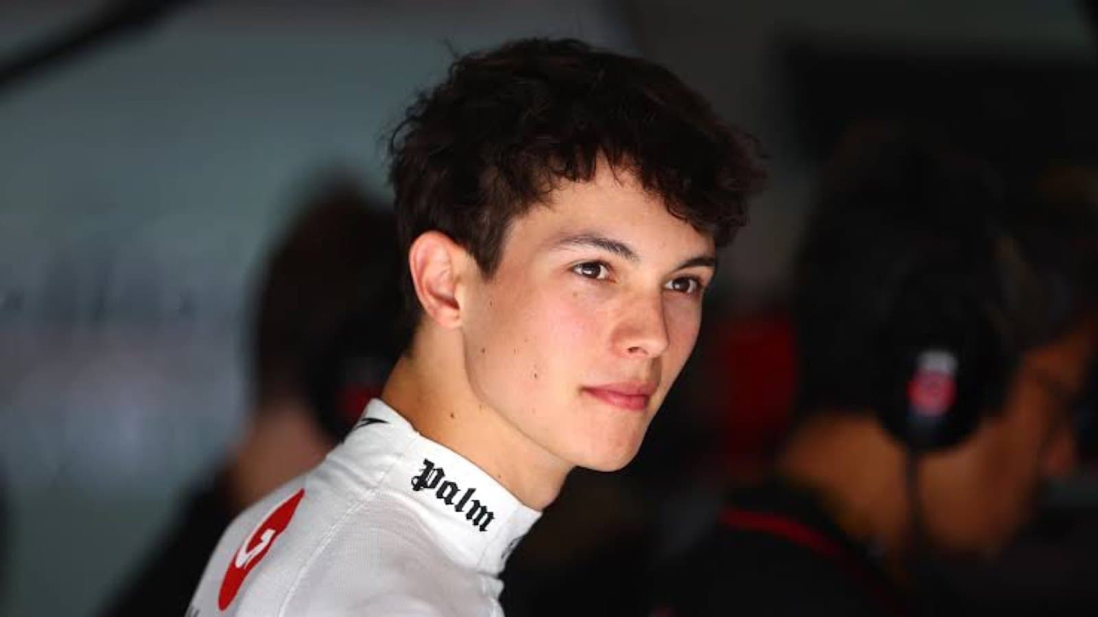 A portrait of Formula 1 driver Ollie Bearman in racing overalls in the paddock.