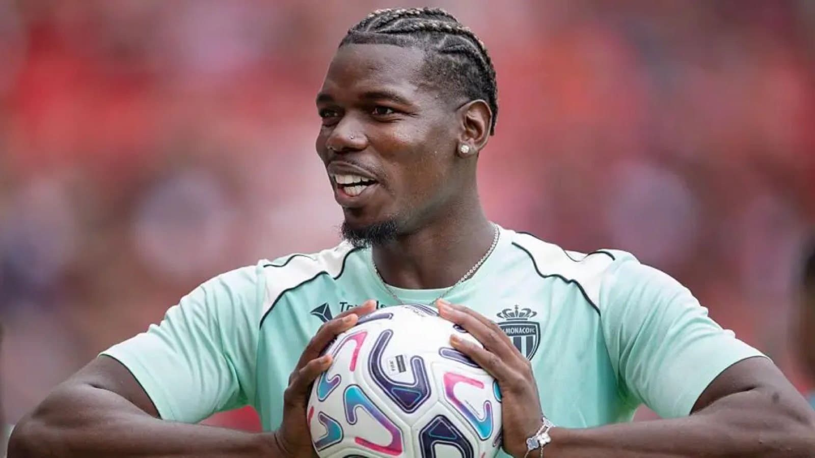 Paul Pogba, smiling and holding a football, wearing an AS Monaco training kit.