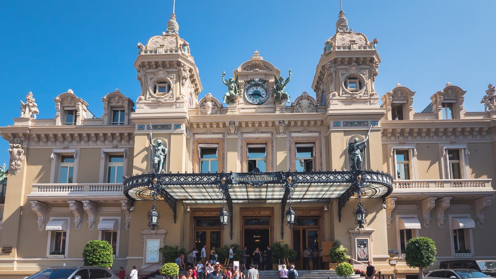 The facade of the Casino de Monte-Carlo in daylight, with a red sports car parked at the entrance.