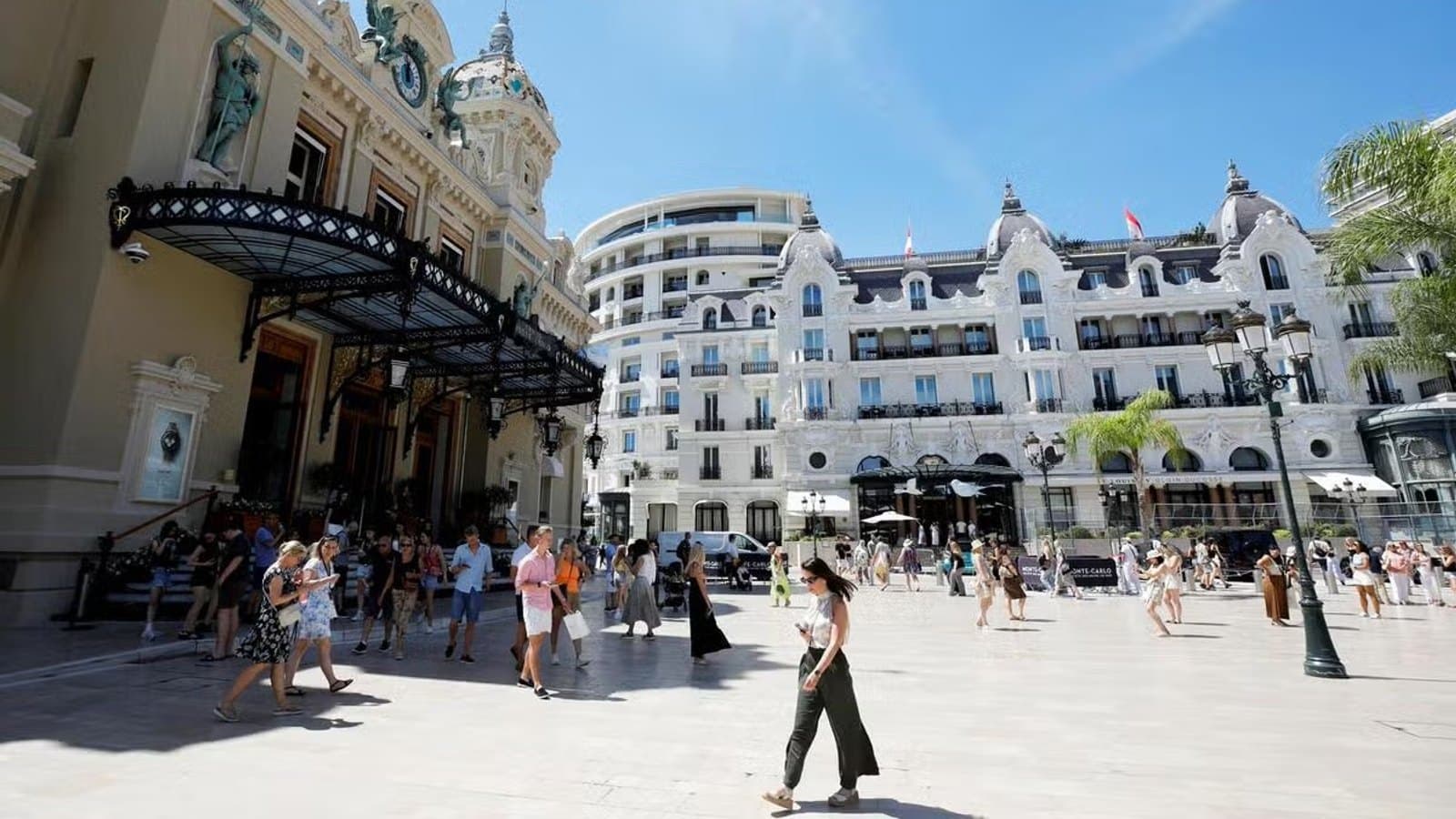 Pedestrians crossing Place du Casino in front of the Casino de Monte-Carlo and Hotel de Paris on a sunny day.