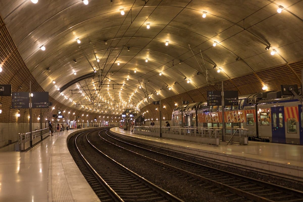 A train at the platform in the vaulted tunnel of a station, with passengers on the platform