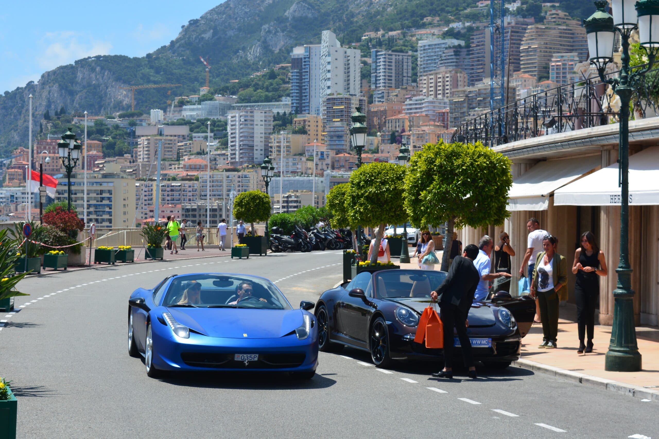 Des supercars circulent sur une avenue de Monaco bordée d'arbres et d'immeubles