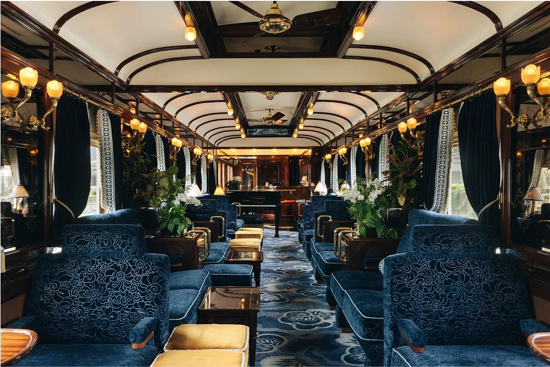 Interior of the Venice Simplon-Orient-Express lounge car, with blue velvet armchairs and a piano